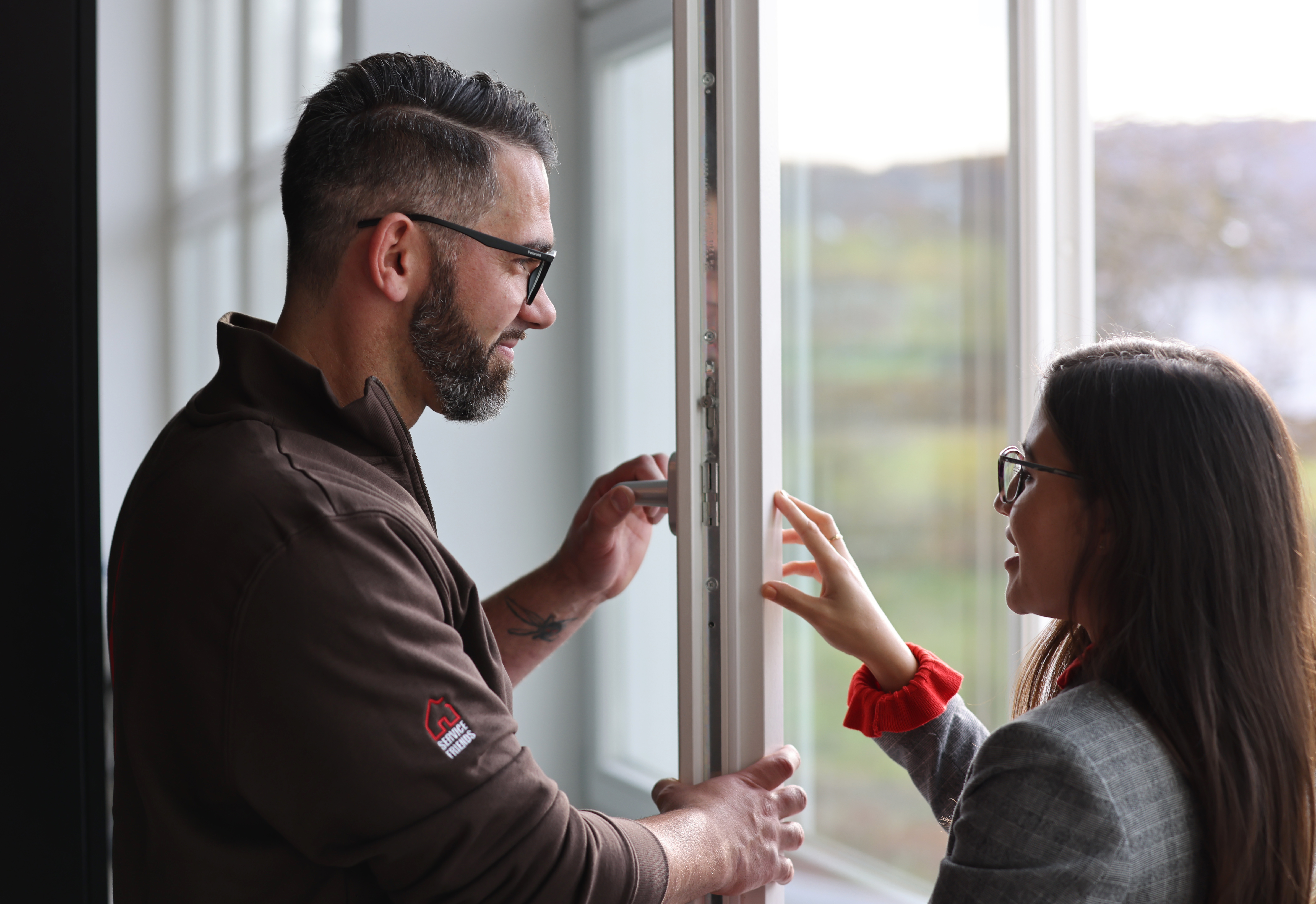 Eine Kundin ist im Gespräch mit einem Servicetechniker, der ein Fenster begutachtet.