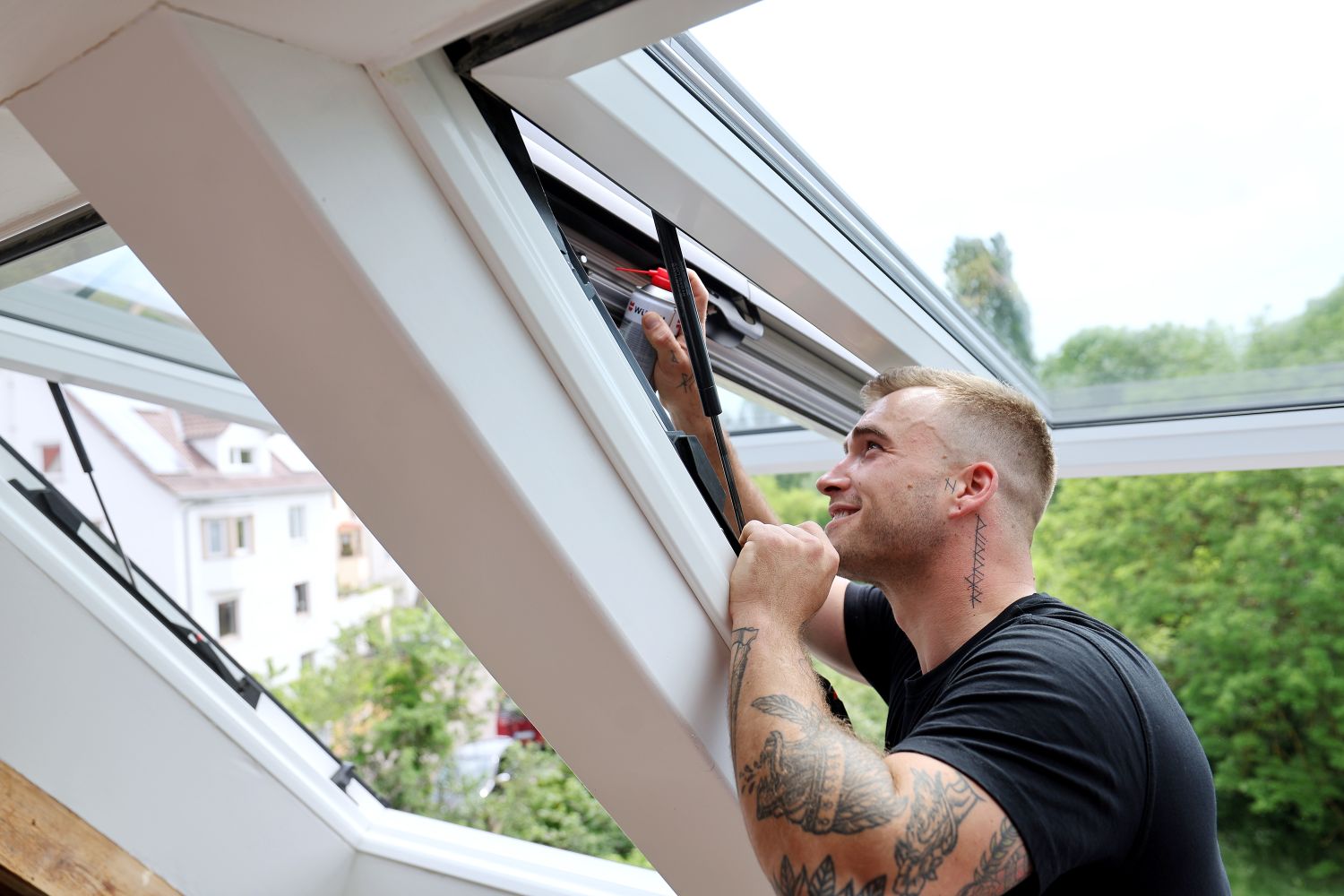 Ein Service-Techniker, der gerade an einem offenen Dachfenster den Beschlag repariert.