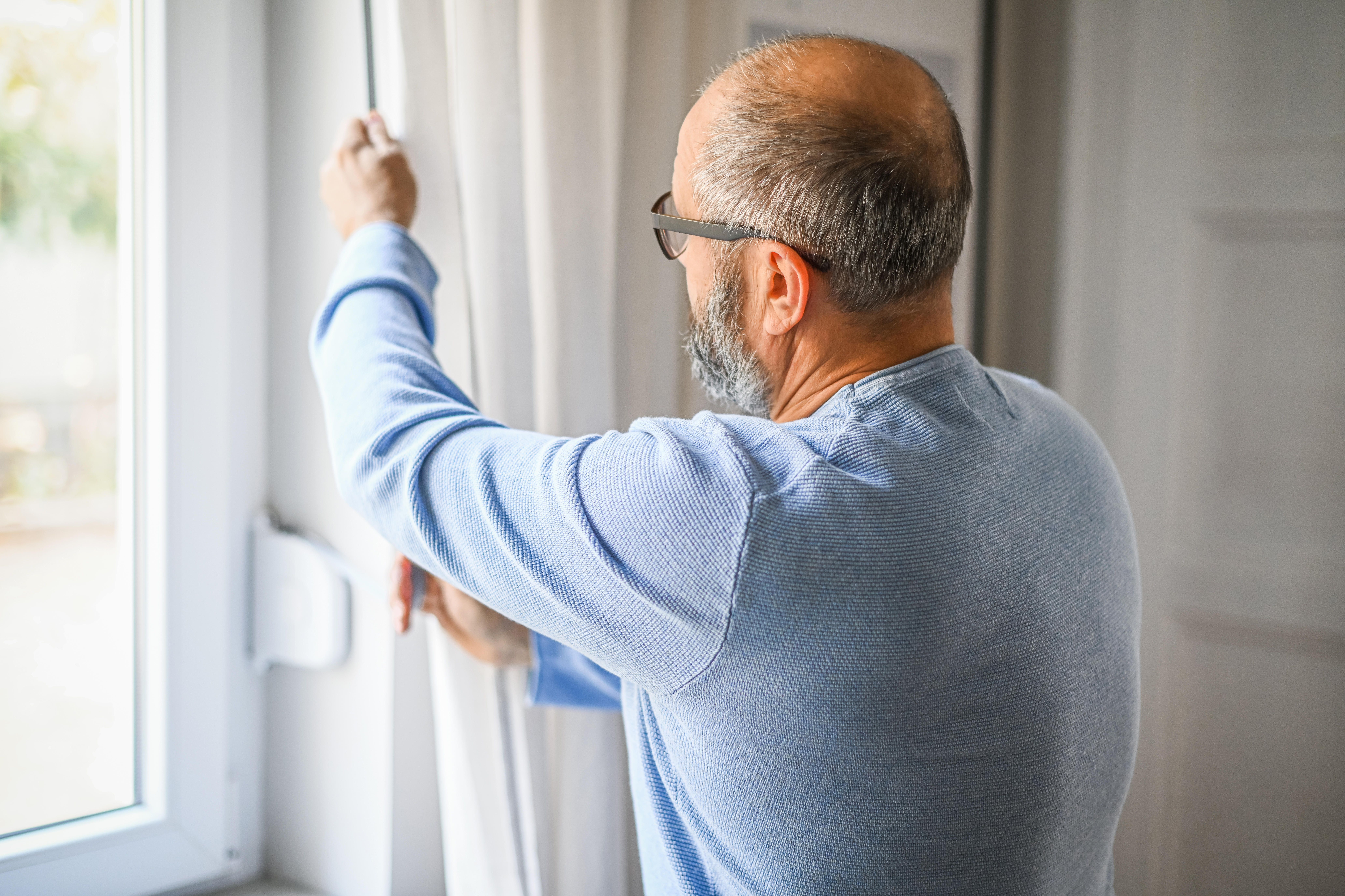 Mann hält Gurtband eines Rollladens am Fenster in der Hand