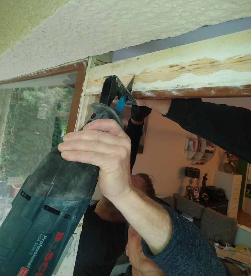 Ein Handwerker verwendet eine elektrische Säge, um den Rahmen eines Fensters zu bearbeiten.