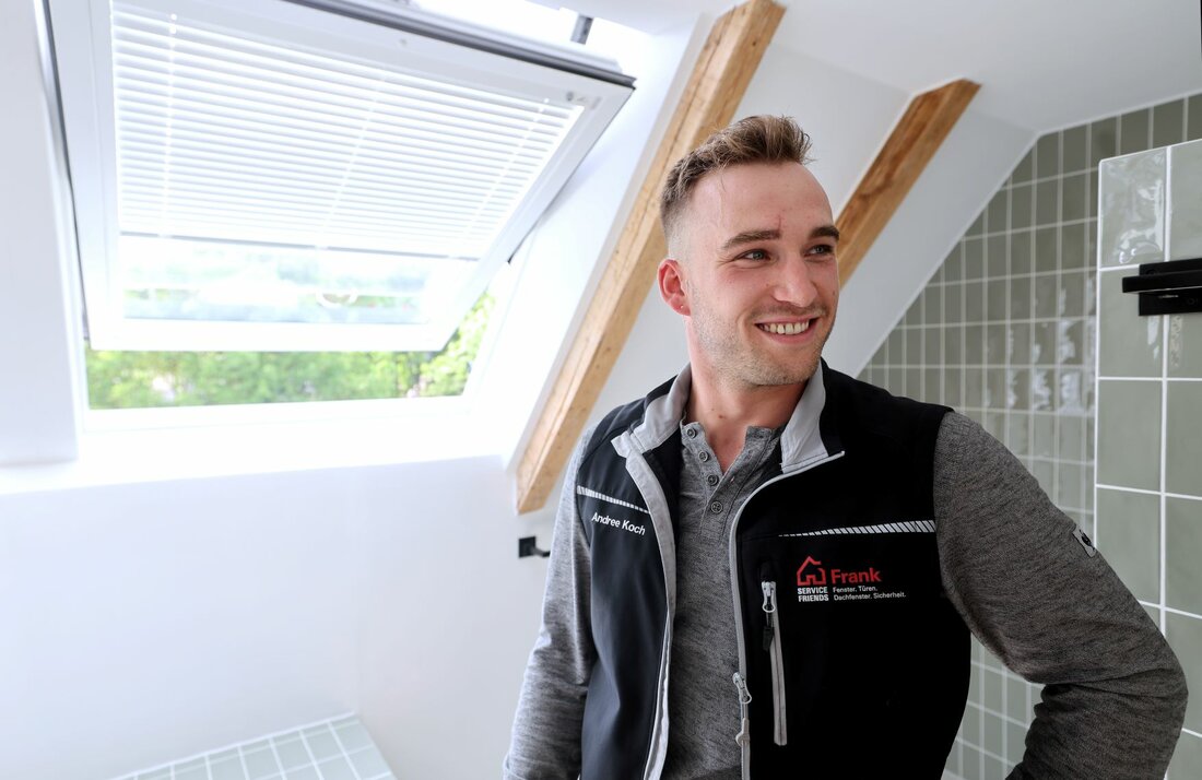 Service-Techniker steht lächelnd vor einem Dachfenster.