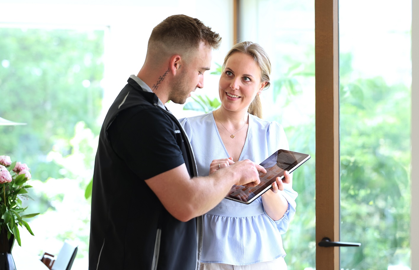 Die Kundin hält ein iPad in der Hand und zeigt es dem Service-Techniker, der etwas darauf antippt. Er erklärt ihr währenddessen etwas dazu.